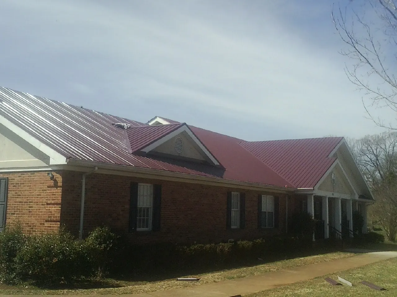 Red metal roof with gabled entries on a long brick building, from a Hail Damage Roof Repair job in Sumner